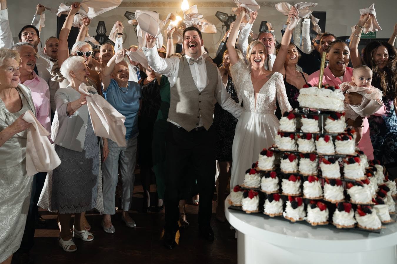 Goście weselni wznoszący toast przy piętrowym torcie