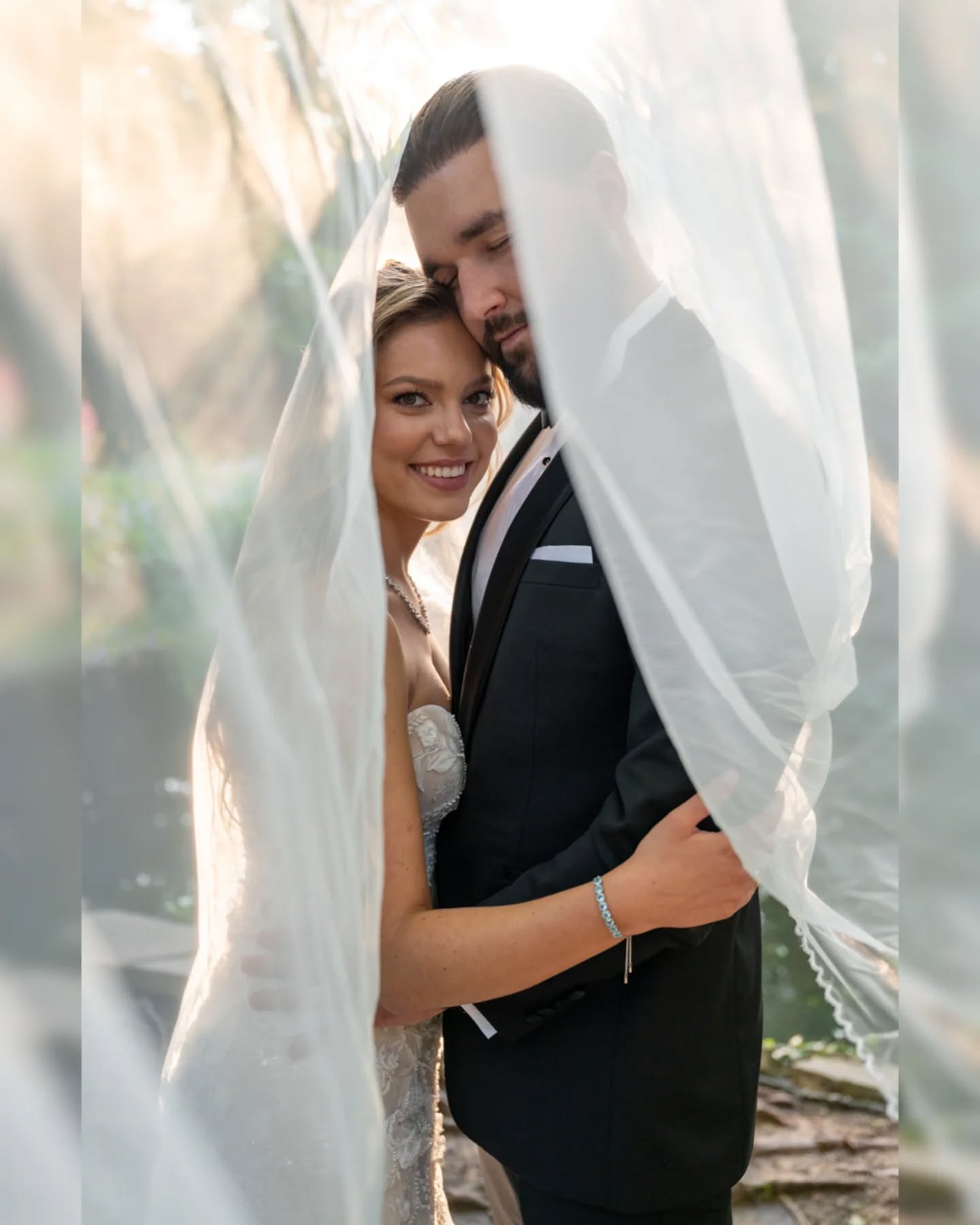 Para młoda przytulona pod uniesionym welonem podczas pleneru